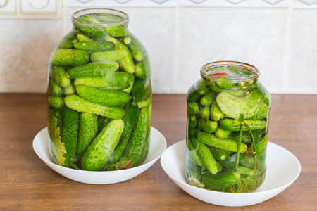 Naturally fermented quick pickled cucumbers in two jars of different sizes during souring on a kitchen tableの写真素材