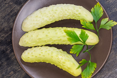 Several freshly harvested whole white cucumbers and parsley twig on the brown dish on a black surface, top viewの写真素材