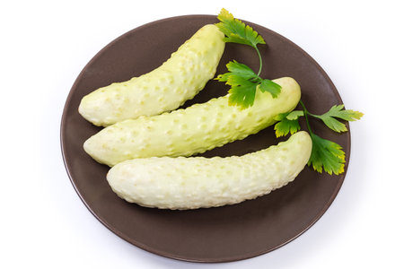 Several freshly harvested whole white cucumbers and parsley twig on the brown dish on a white backgroundの写真素材