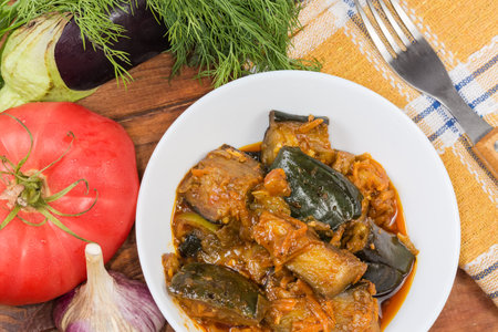Eggplant pieces stewed with other vegetables in the bowl among the raw ingredients for their preparation on the rustic table, top viewの写真素材
