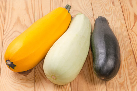 Whole raw freshly harvested dark green zucchini, yellow and light green vegetable marrows on the rustic tableの写真素材