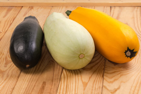 Whole raw dark green zucchini, yellow and light green vegetable marrows on the wooden surface, close-up in selective focusの写真素材