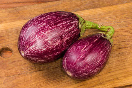 Two whole ripe eggplants teardrop in shape with purple and white stripes, so-called Graffiti eggplants on a wooden cutting board, close-upの写真素材