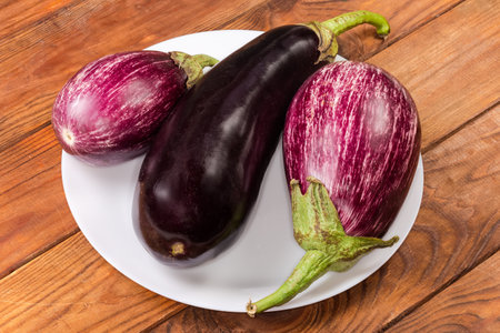 Raw whole conventional eggplant and striped, so-called Graffiti eggplants on the white dish on a rustic tableの写真素材