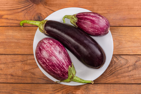 Raw whole conventional eggplant and striped, so-called Graffiti eggplants on the white dish on a rustic table, top viewの写真素材