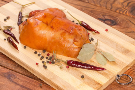 Boiled-smoked pork ham hock among the different dried spices on the wooden cutting board, close-up in selective focusの写真素材