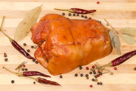 Boiled-smoked pork ham hock among the different dried spices and red chili pods on the wooden cutting boardの写真素材