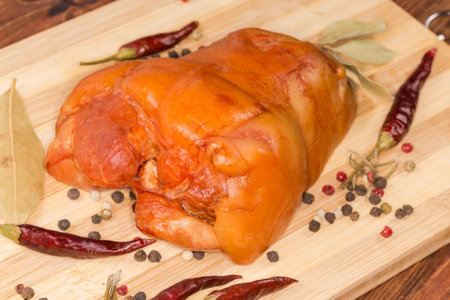 Boiled-smoked pork ham hock among the different dried spices on the wooden cutting board, close-up in selective focusの写真素材