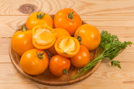 Whole ripe yellow tomatoes, two halves of the same tomato and twigs of fresh parsley on the wooden dish on the rustic tableの写真素材