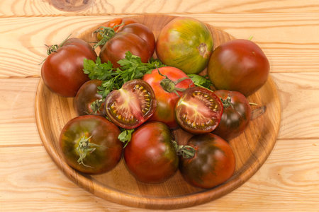 Two halves of the ripe green-brown tomato kumato lie on the same whole tomatoes with twigs of fresh parsley on the wooden dish on the rustic tableの写真素材