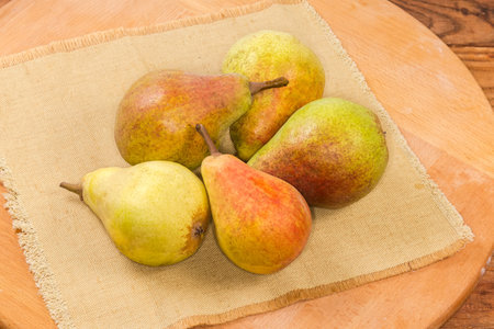 Whole ripe freshly harvested green with red sides pears on the textile napkin on a round wooden boardの写真素材