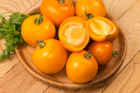 Whole and halves of the ripe yellow tomatoes with twigs of fresh parsley on the wooden dish on the rustic table close-upの写真素材