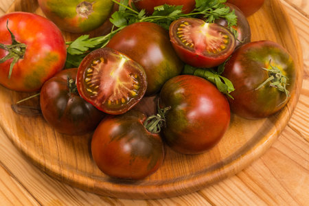 Two halves of the ripe green-brown tomato kumato lie on the same whole tomatoes on the wooden dish on the rustic table, fragment close-upの写真素材