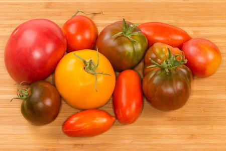 Freshly ripe whole varicolored tomatoes of different varieties on the wooden cutting boardの写真素材