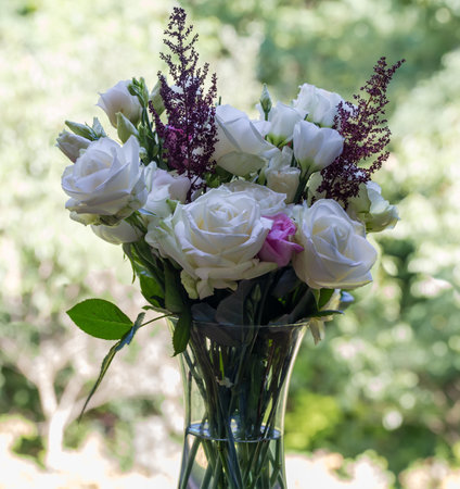 Bouquet of the white roses and white eustoma in glass transparent flower vase with water on a green blurred backgroundの写真素材