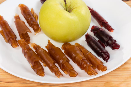 Thin soft flexible pastila made with dried apple puree and rolled into tubes against the whole fresh apple on the dish, close-upの写真素材