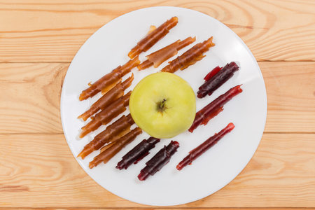 Thin soft flexible pastila made with dried apple puree and rolled into tubes around the whole fresh apple on the dish on rustic table, top viewの写真素材