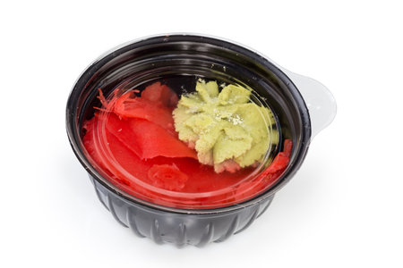 Sliced pickled ginger and wasabi sauce in the small plastic container closed with trahsparent lid on a white backgroundの写真素材
