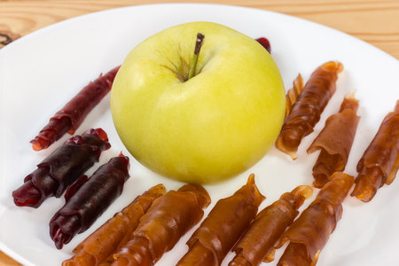 Thin soft flexible pastila made with dried apple puree and rolled into tubes around the whole fresh apple on the dish, close-up in selective focusの写真素材