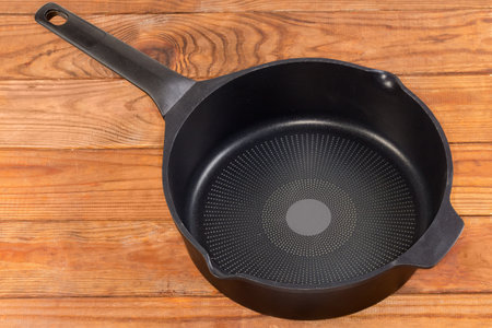 Empty deep frying pan made of cast aluminum with titanium non-stick coating and opposite helper handle on the rustic tableの写真素材