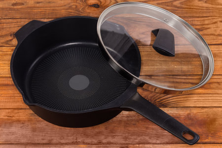 Empty deep frying pan made of cast aluminum with titanium non-stick coating with partly removed lid of glass and stainless steel on the rustic tableの写真素材