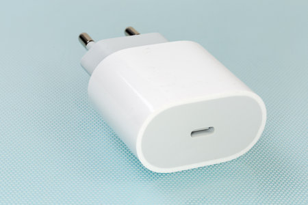 White charger with USB Type-C output socket for batteries charging of portable electronic accessories, close-up on a blue surfaceの写真素材