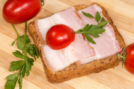 Open sandwich with slices of the boiled-smoked pork belly on skin and cherry tomatoes on the cutting board close-upの写真素材