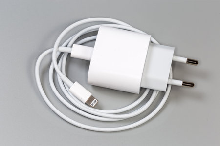 White charger with AC Euro plug and Lightning cable connected to the output socket for batteries charging of portable electronic accessories, top view on a gray backgroundの写真素材