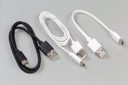 Black and two different white USB cables with plugs standard A and standard C at the cables ends on a gray backgroundの写真素材
