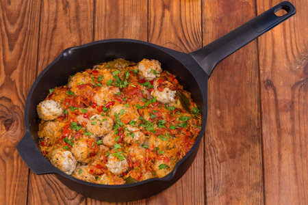 Rice meatballs stewed with red tomato sauce in the deep frying pan on the rustic tableの写真素材