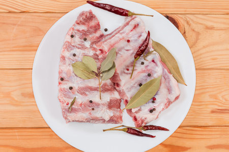 Two pieces of the raw pork ribs with dried spices on the white dish on the rustic table, top viewの写真素材