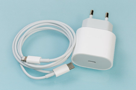 White charger with USB Type-C output socket for batteries charging of portable electronic accessories and appropriate cable, close-up on the blue surfaceの写真素材