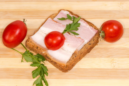 Open sandwich with slices of the boiled-smoked pork belly on skin and cherry tomatoes on the cutting boardの写真素材