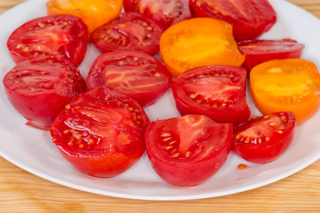 Halves of ripe red and yellow tomatoes on the white dish on the rustic table, side view of fragment close-up in selective focusの写真素材