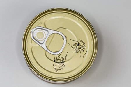 Sealed circular food tin can with ring-pull tab for easy opening lid and designation of opening method, top view on a gray surfaceの写真素材