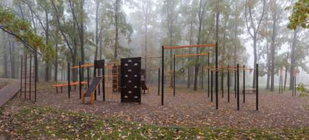 Empty public outdoor sports area with equipment for free athletic workout and fitness among the trees of the autumn foggy park, panoramic viewの写真素材