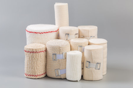 Set of modern woven elastic medical bandages different sizes rolled into rolls, some of them with aluminum stretchable clips stand on a gray surface, side view close-upの写真素材