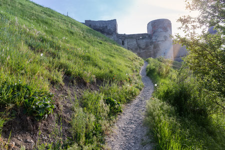 Steep walking path on a hillside leading to the ancient fortress of the 14-18th centuries, view of the southwestern wall and towers against the sky backlit, Kamianets-Podilskyi, Ukraine.のeditorial素材