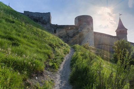 Steep walking path on a hillside leading to the ancient fortress of the 14-18th centuries, view of the southwestern wall and towers against the sky backlit, Kamianets-Podilskyi, Ukraine.のeditorial素材