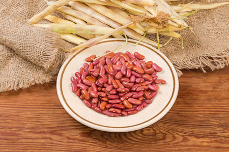 Raw husked red kidney beans on the saucer against the same beans in the pods on burlap on the rustic...