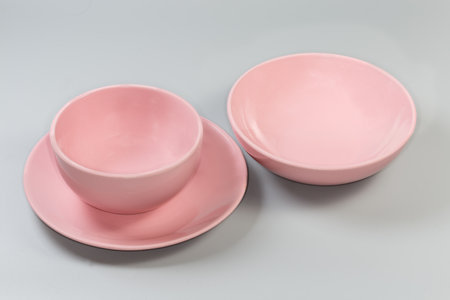 Empty glazed ceramic pink deep bowl for serving food and dining on the flat service plate and wide shallow bowl separately on a gray backgroundの写真素材