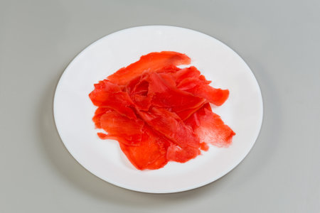 Red pickled thinly sliced ginger on the white dish on a gray background