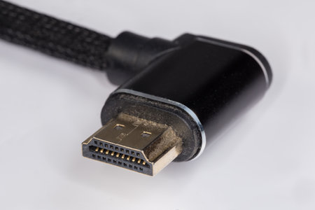Full-size L-shaped dusty HDMI connector at the edge of an used high quality HDMI cable in shielded metal braided sleeving on a light surface, close-up in selective focusの写真素材