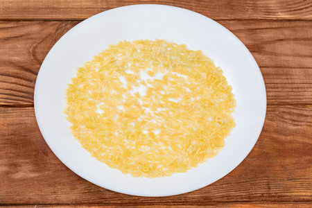 Raw pasta in shape of capital letters of English alphabet and Arabic numerals poured onto a white dish on the rustic table, top viewの写真素材