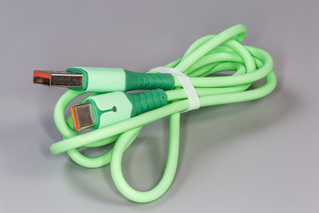 Twisted green USB cable with plugs standard A and standard C at the edges on a gray surface, close-up in selective focusの写真素材