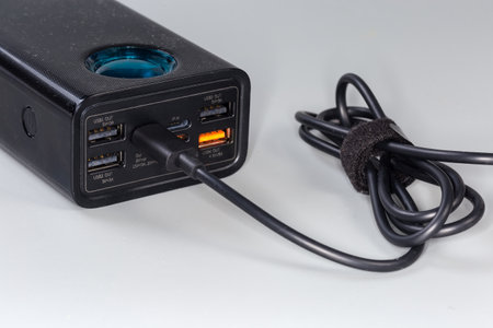 Front panel of the power bank with connected USB cable, input and output USB ports and ports of other standards with designation of standards and parameters on the front panel on a gray backgroundの写真素材