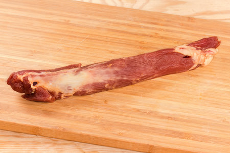 Whole dry-cured pork tenderloin on the wooden bamboo cutting board close-upの写真素材