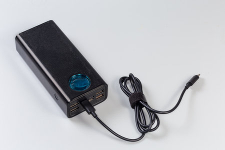 Power bank with connected USB cable, input and output USB ports and ports of other standards with designation of standards and parameters on the front panel on a gray backgroundの写真素材