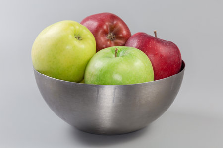Whole green, yellow and red apples in the stainless steel kitchen bowl on a gray background, side viewの写真素材