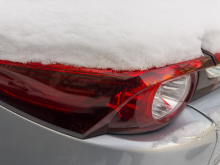 Fragment of rear of parked gray car with tail lamps and brake lights block, covered with fluffy snow above, close-up in overcast weatherの写真素材